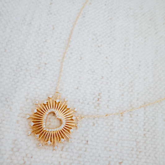 Gold necklace with a heart-shaped pendant on a textured white background