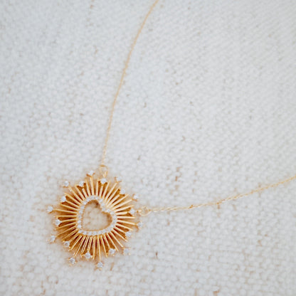 Gold necklace with a heart-shaped pendant on a textured white background