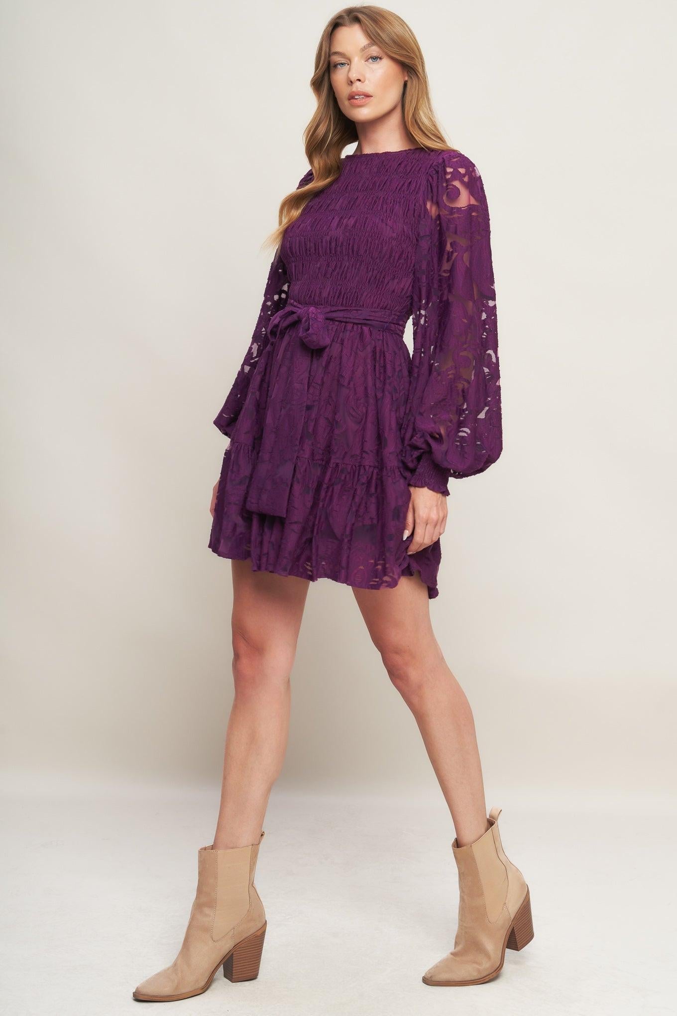 Woman wearing a purple lace dress with beige boots on a white background