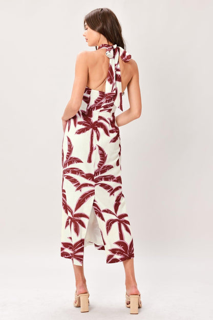 Woman wearing a white jumpsuit with red palm leaf pattern on a plain background
