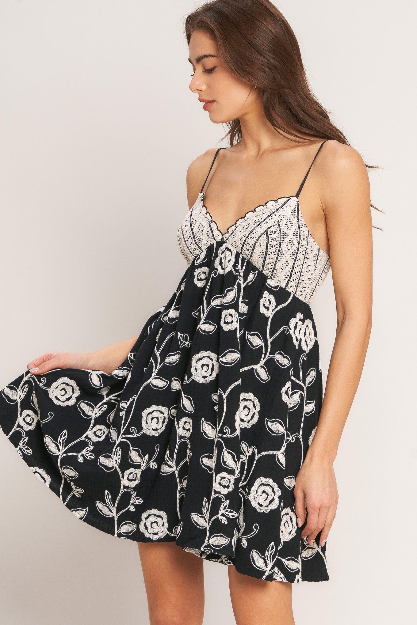 Woman wearing a black floral dress with white lace trim on a plain background