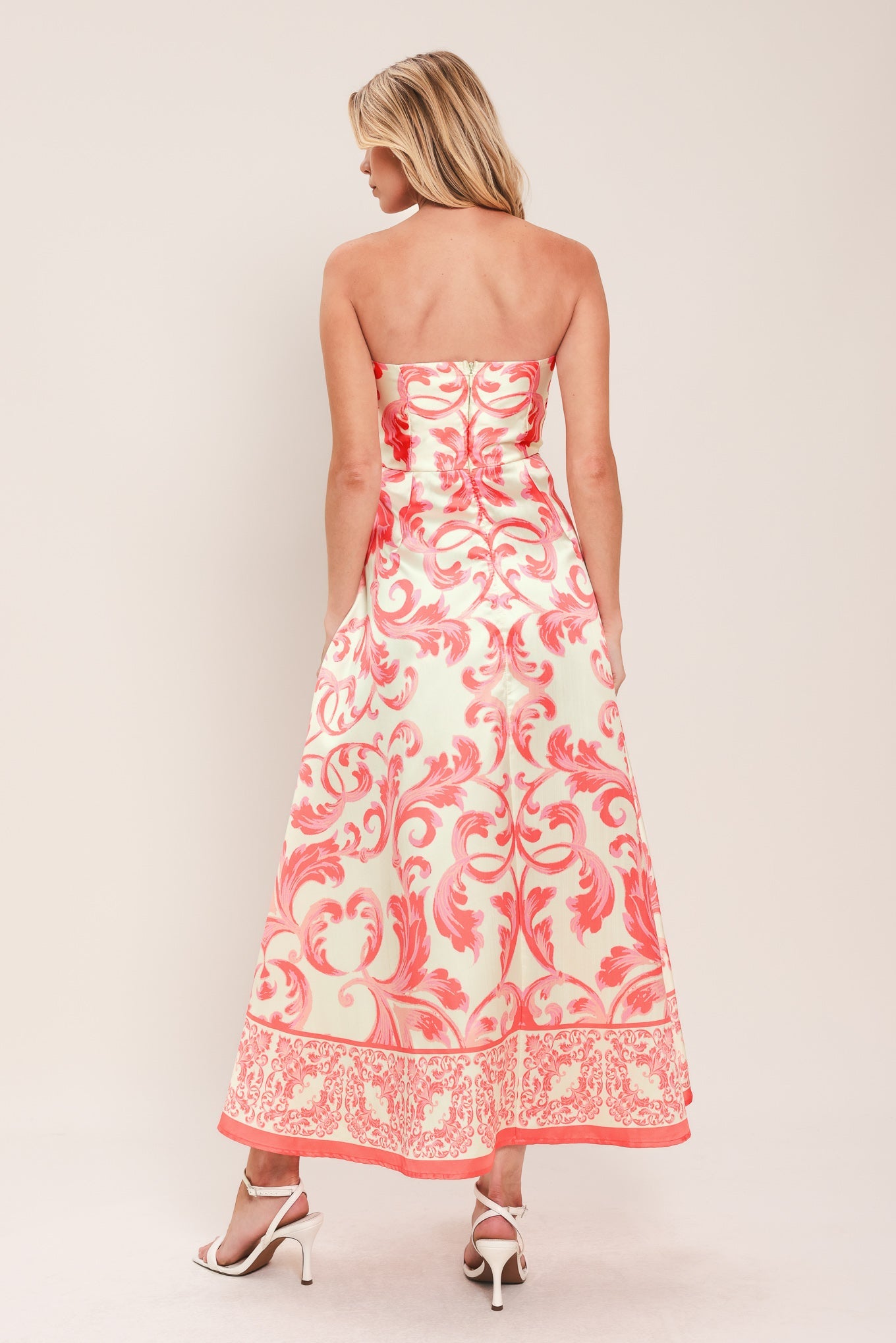Woman wearing a strapless floral dress with pink and white pattern on a plain background