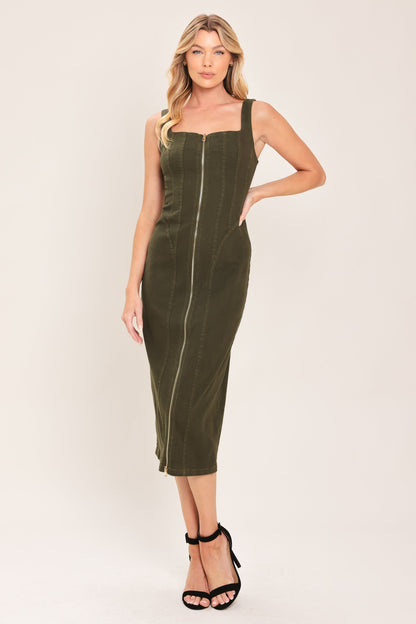 A woman modeling an olive green sleeveless midi dress with a square neckline, front zipper, and side pockets, paired with black strappy high-heeled sandals against a plain light beige studio background.