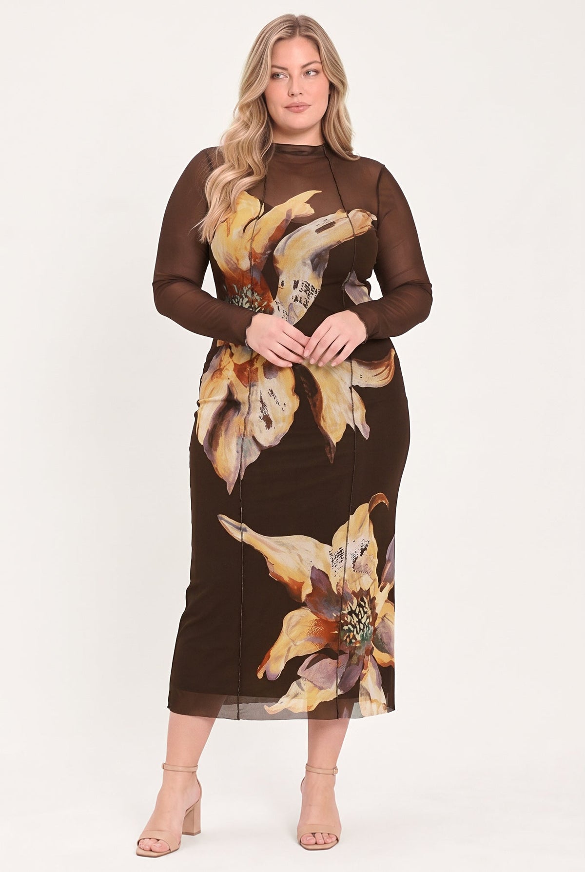 A woman modeling a brown long-sleeve midi dress with sheer mesh sleeves and a large yellow and beige floral print, paired with beige high-heeled sandals against a plain white studio background.