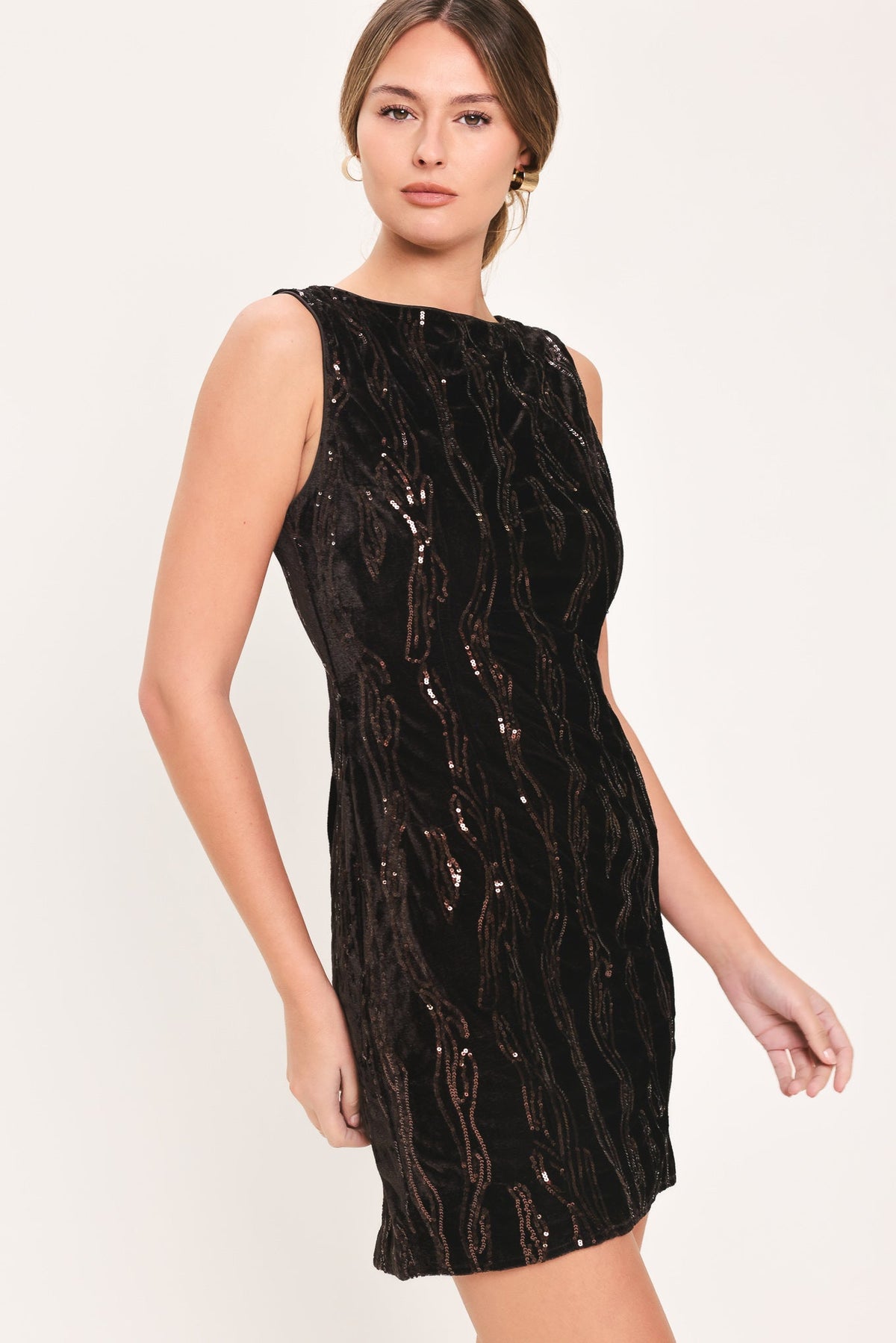 A woman modeling a sleeveless black sequined mini dress with a textured, wavy pattern of reflective sequins, set against a plain light background.