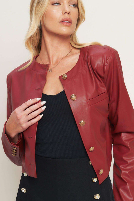 Woman wearing a red leather jacket with gold buttons on a plain background