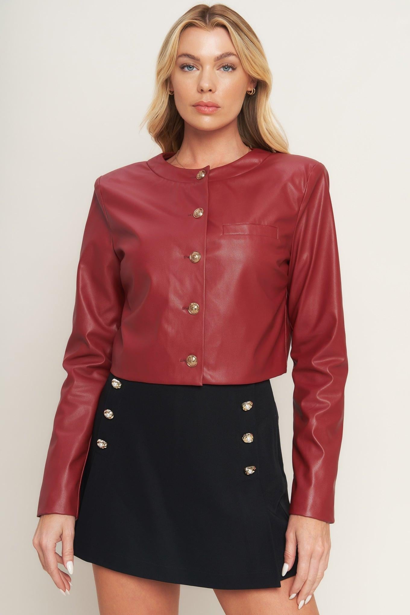 Woman wearing a red leather jacket with gold buttons on a plain background