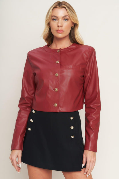 Woman wearing a red leather jacket with gold buttons on a plain background