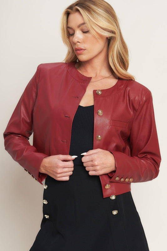 Cropped red leather jacket with gold buttons on the front and cuffs, worn over a black top and skirt.