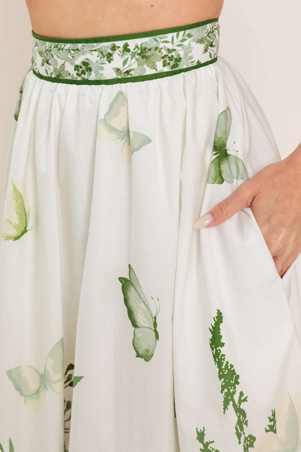 White dress with green butterfly pattern and green waistband on a white background