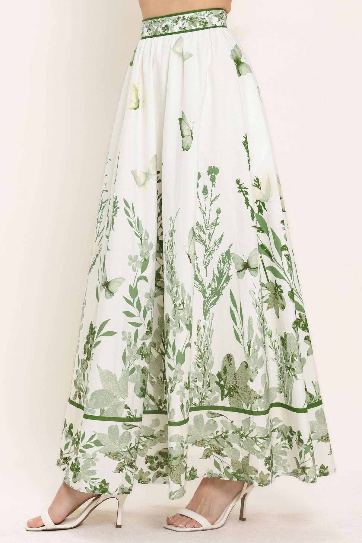 Long white skirt with green floral pattern worn by a model on a plain background