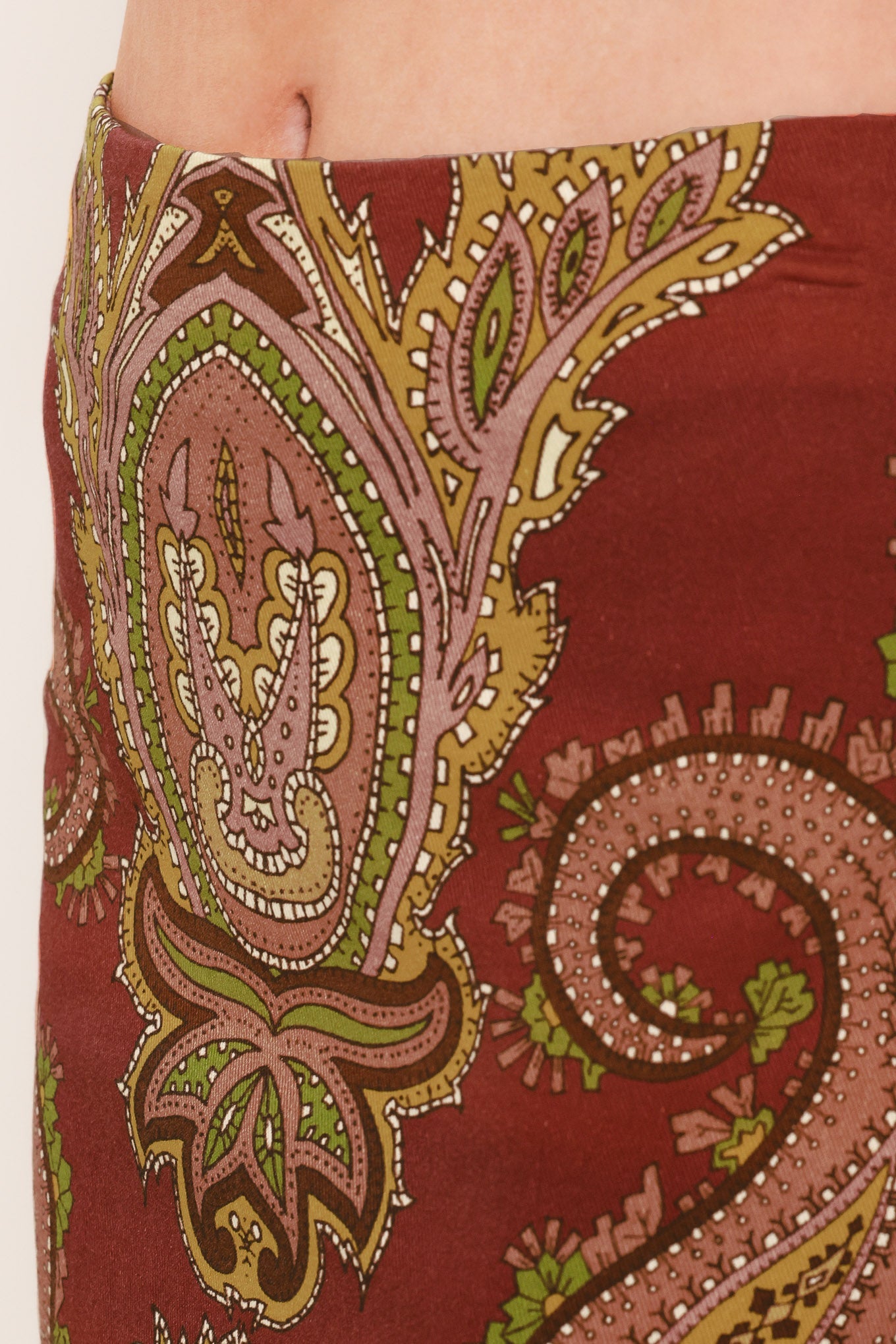 A close-up of a skirt or wrap skirt featuring a detailed paisley pattern in rust red, dusty pink, olive green, and gold, worn by a model.