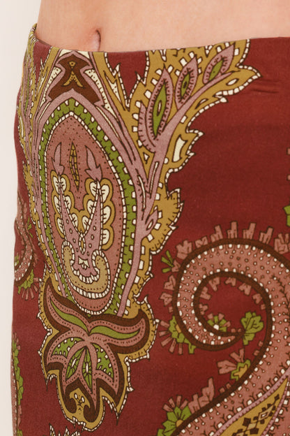 A close-up of a skirt or wrap skirt featuring a detailed paisley pattern in rust red, dusty pink, olive green, and gold, worn by a model.