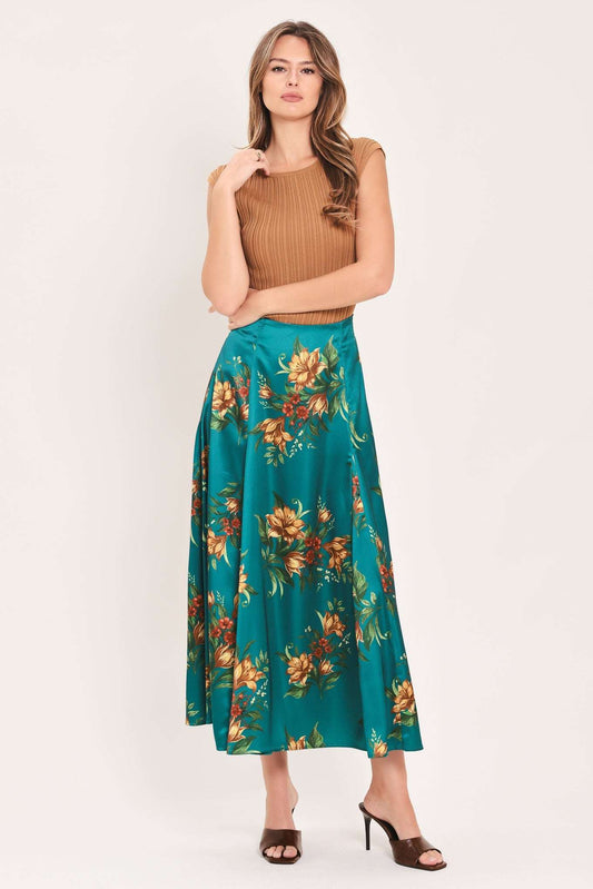 A woman modeling a sleeveless brown ribbed knit crop top and a teal green midi skirt with a large orange and yellow floral print, paired with brown heeled sandals, against a plain off-white studio background.