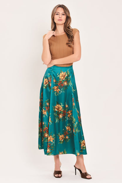 A woman modeling a sleeveless brown ribbed knit crop top and a teal green midi skirt with a large orange and yellow floral print, paired with brown heeled sandals, against a plain off-white studio background.