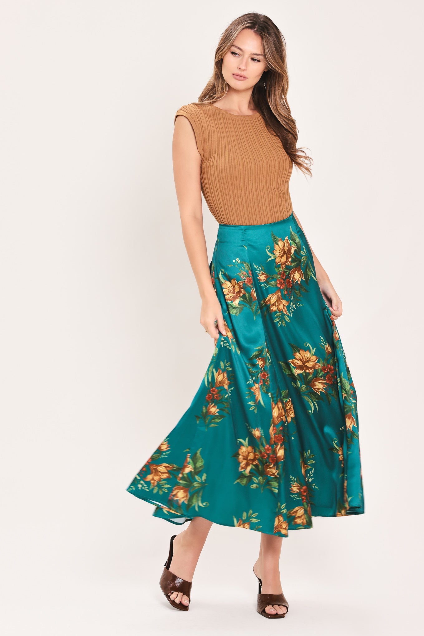 A woman modeling a sleeveless ribbed tan top and a high-waisted teal maxi skirt with a large orange and yellow floral print, set against a plain light background.