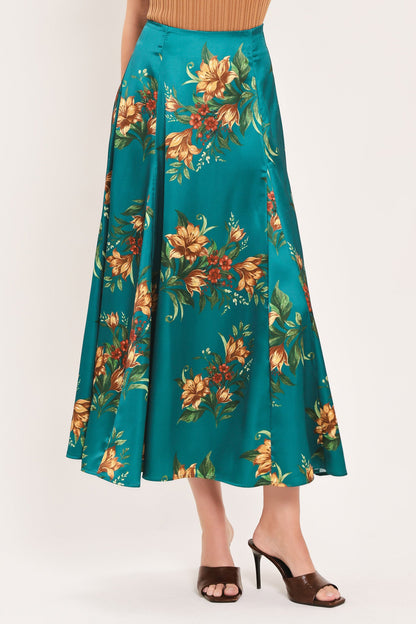 A teal green midi skirt with a vibrant orange and yellow floral print, worn by a model with brown heeled sandals against a plain light background.