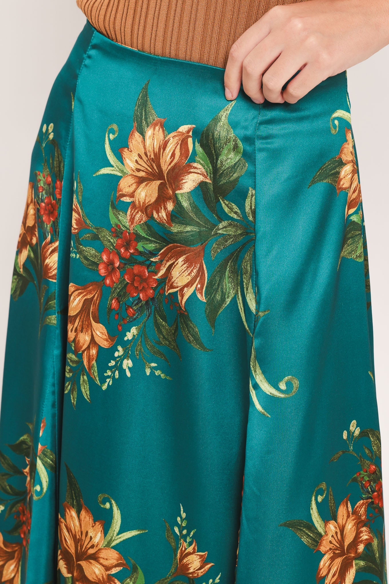 A close-up of a teal satin skirt with a large orange and green floral print, worn with a ribbed brown top. A hand is visible at the waistband.