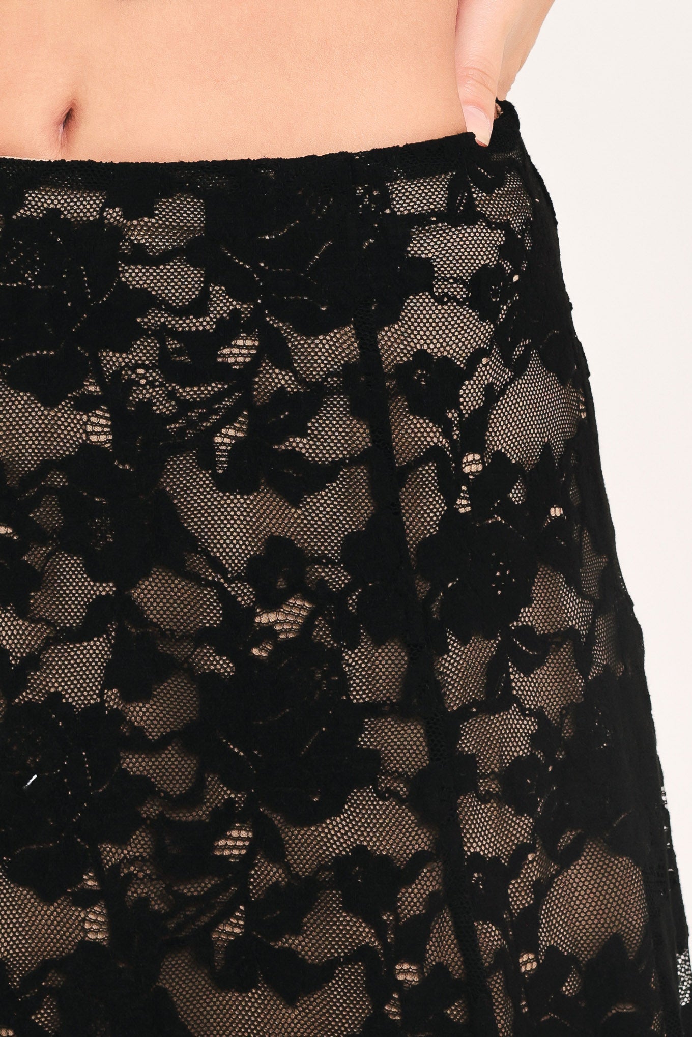 Close-up of a black sheer floral lace garment worn by a model, showing the fabric texture and waistband against a plain light background.
