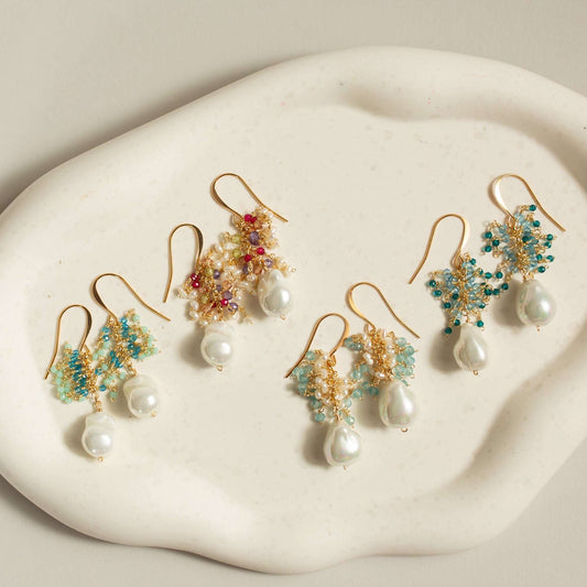 Set of gold earrings with pearls and gemstones on a white stone surface