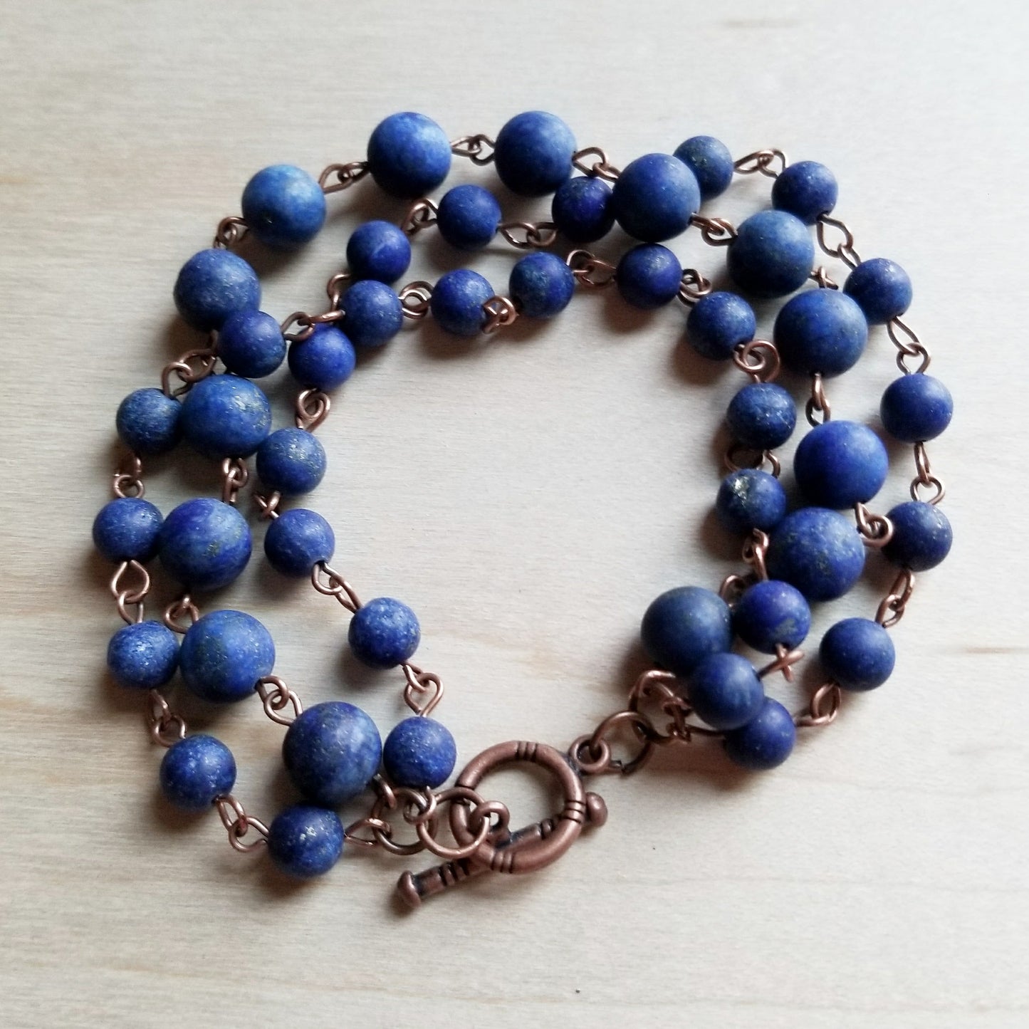 Blue beaded necklace with copper accents on a light wooden surface