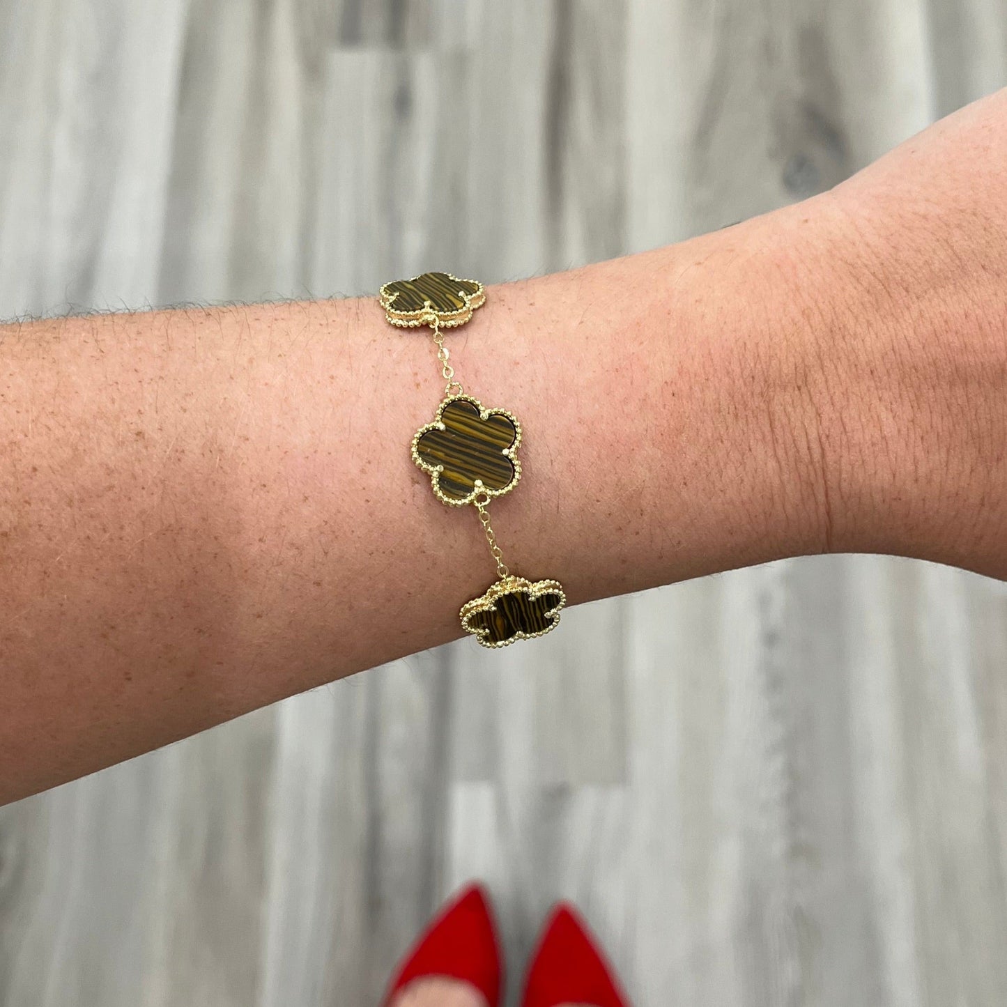 Gold bracelet with clover-shaped charms on a wrist against a neutral background