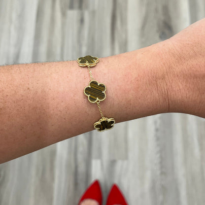 Gold bracelet with clover-shaped charms on a wrist against a neutral background