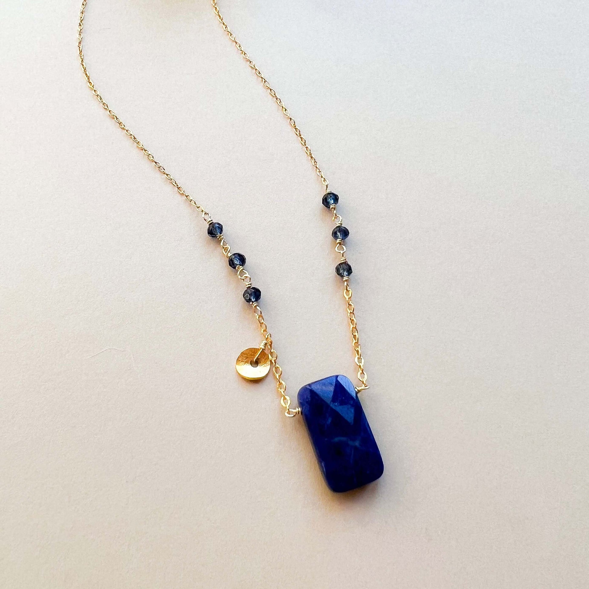 Necklace with blue pendant and gold chain on a light background