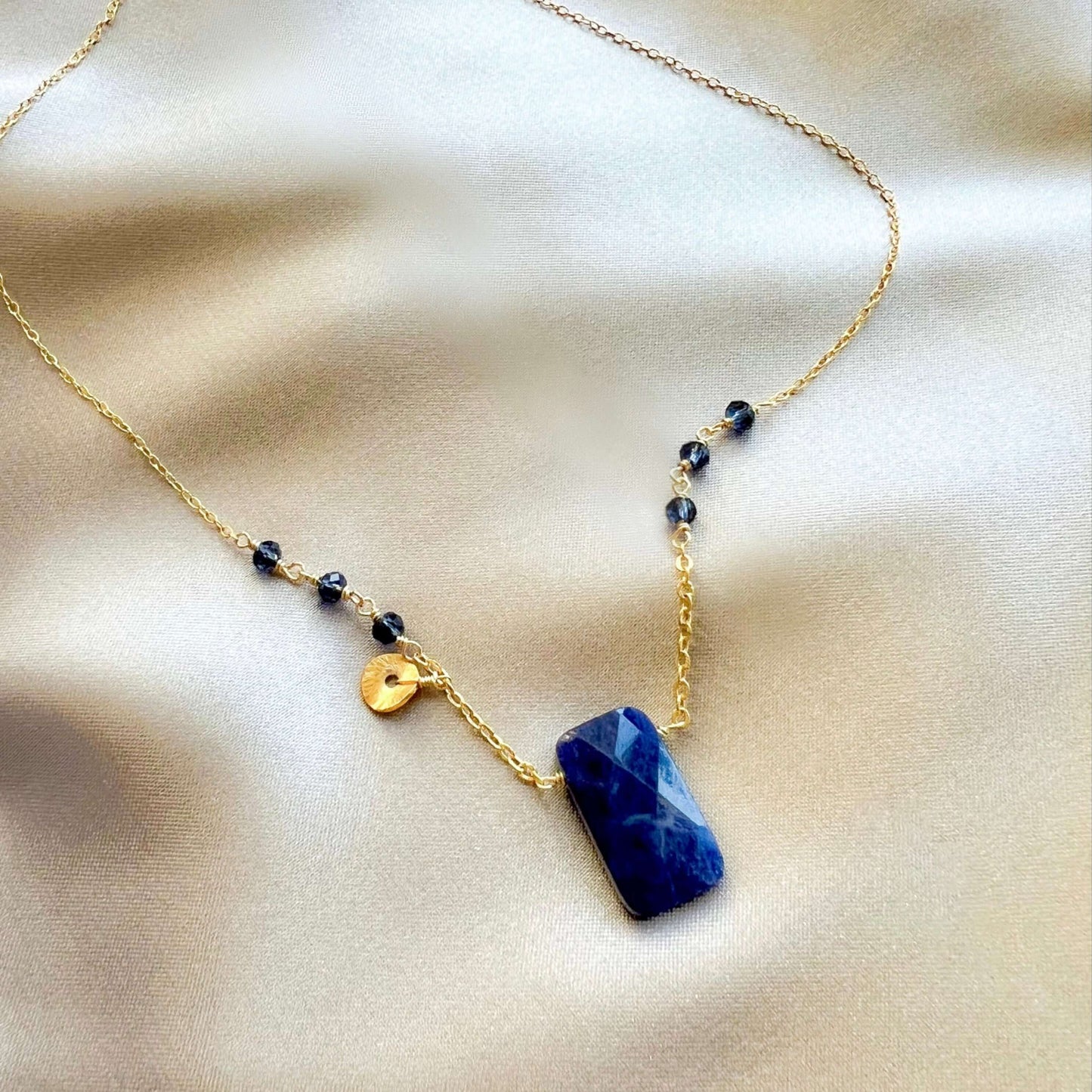 Necklace with a blue pendant and gold chain on a beige fabric background