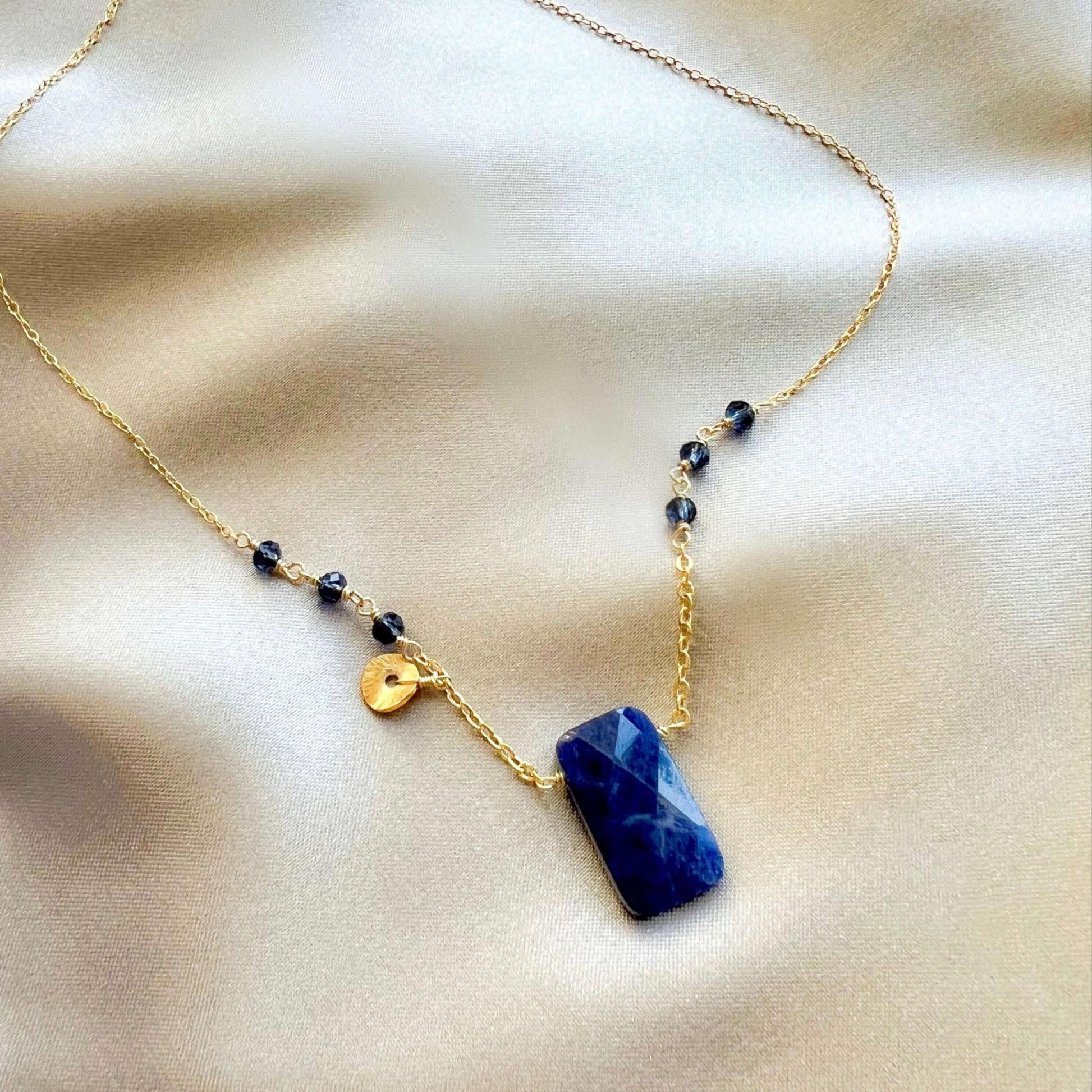 Necklace with a blue pendant and gold chain on a beige fabric background