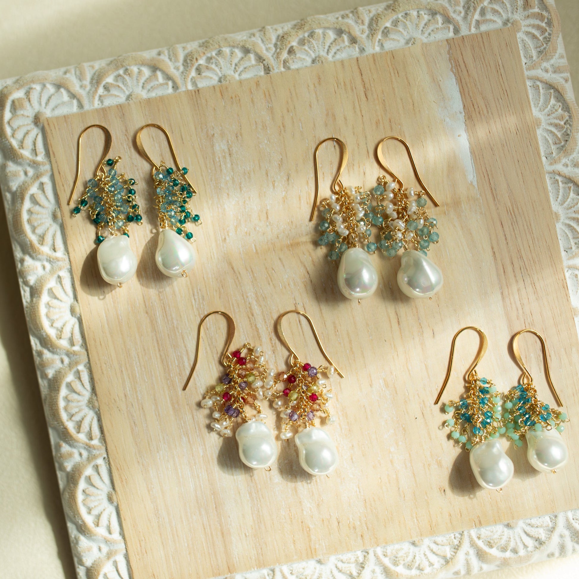 Set of pearl and gemstone earrings on a decorative wooden board.