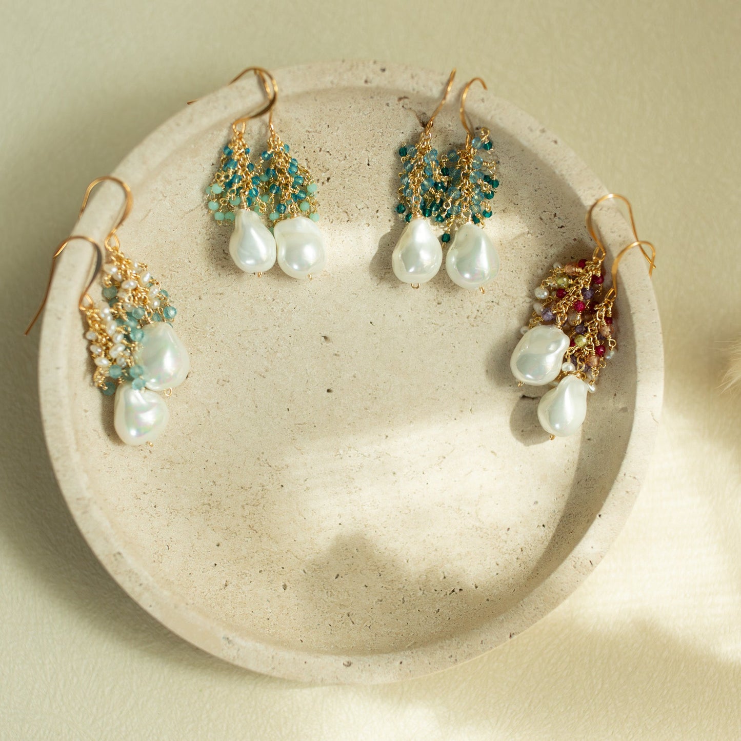 Set of pearl and gemstone earrings on a textured stone surface