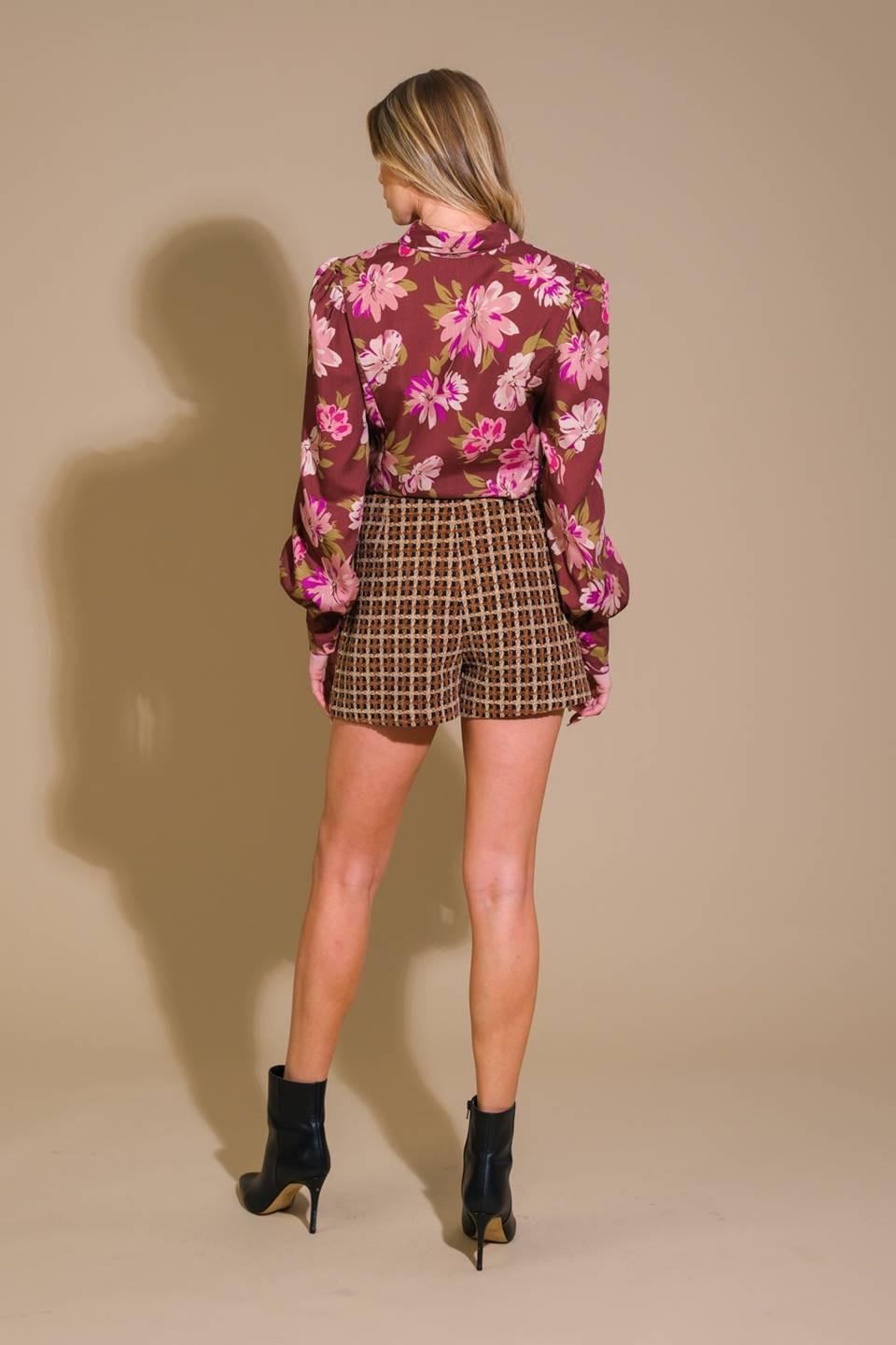 Woman wearing a floral blouse and checkered shorts on a beige background