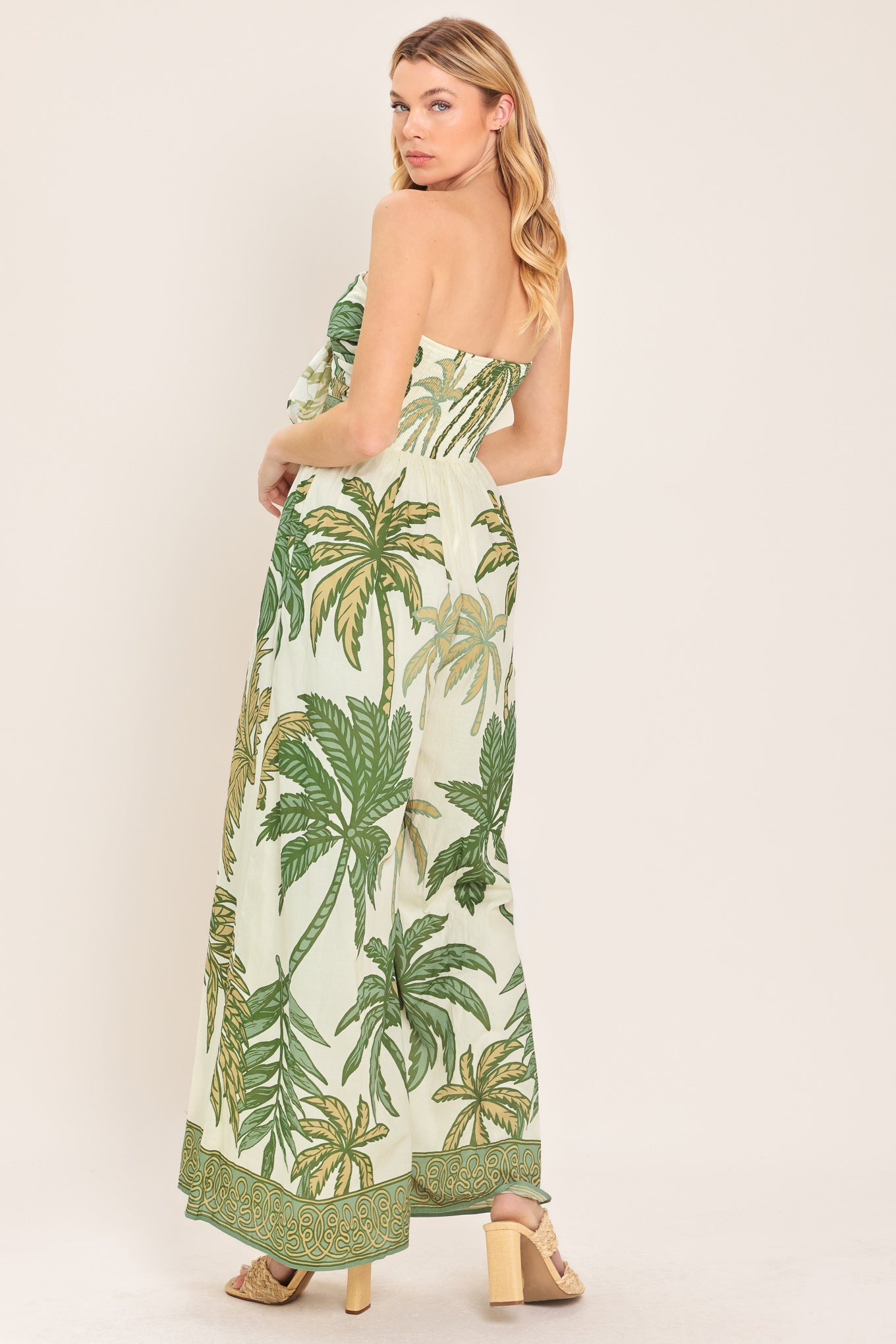 Woman wearing a strapless dress with palm tree pattern on a plain background