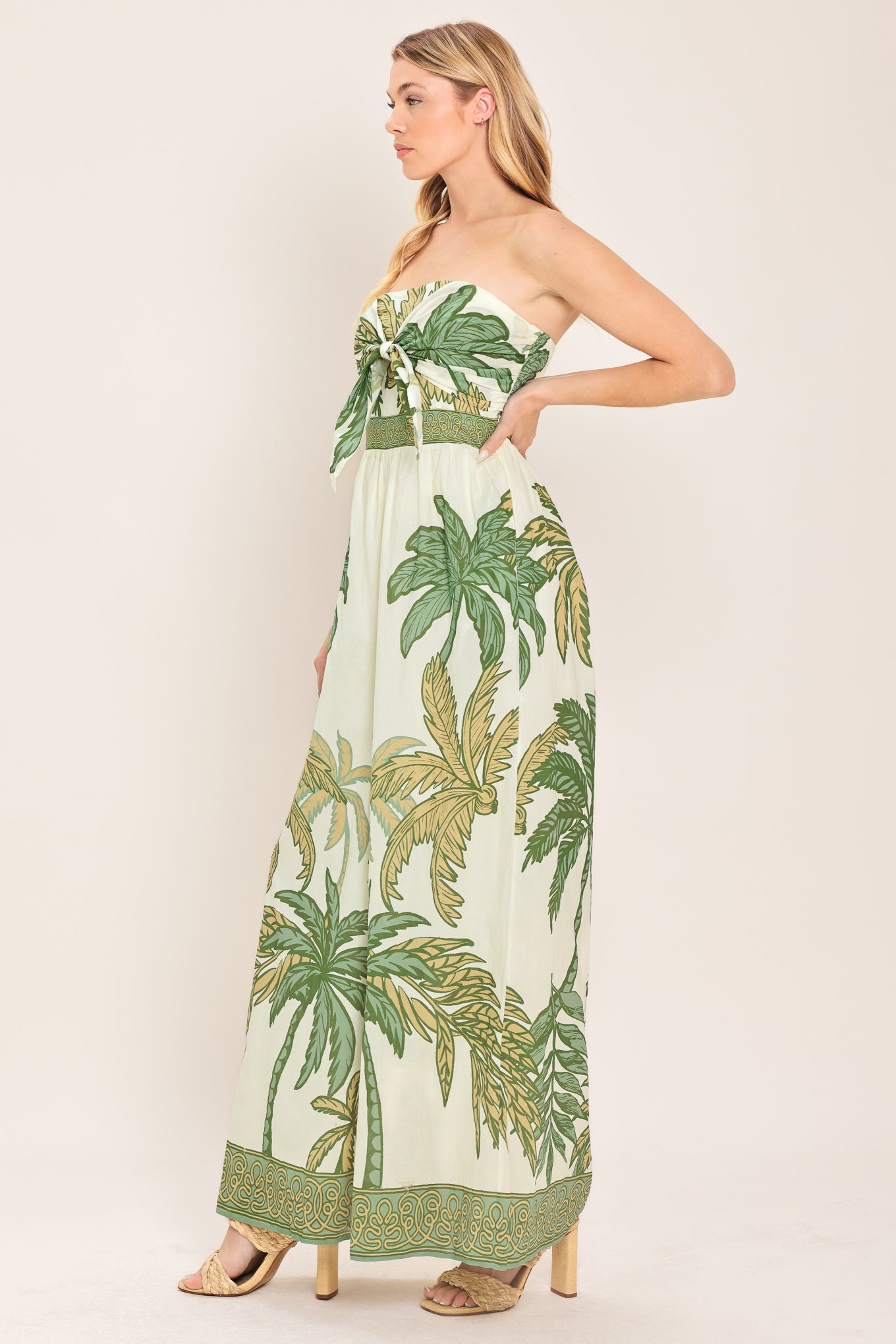 Woman wearing a strapless dress with palm tree pattern on a plain background