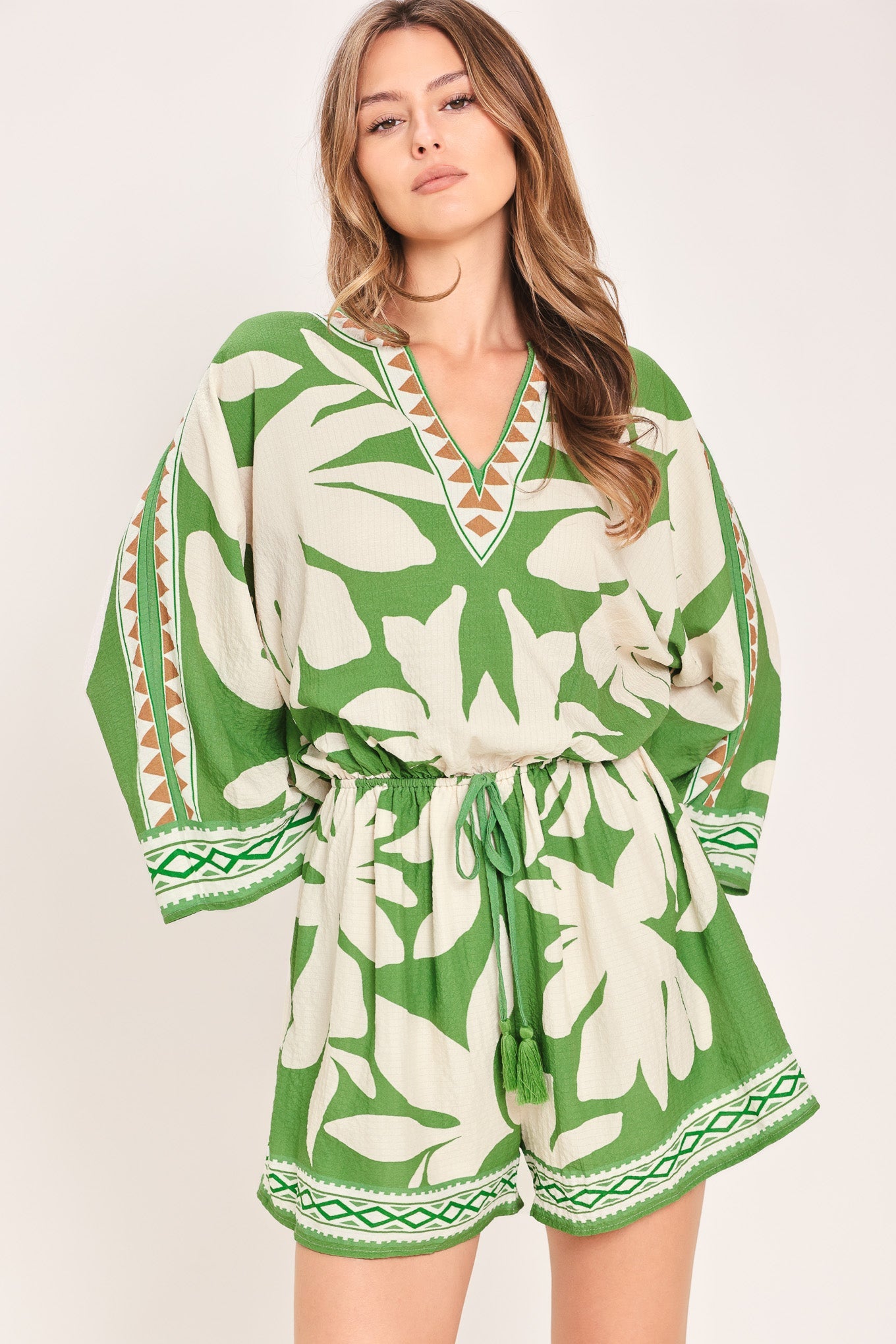 Woman wearing a green and white patterned romper on a plain background