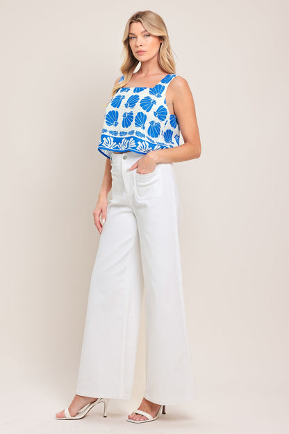 Woman wearing a blue and white patterned top with white pants on a beige background