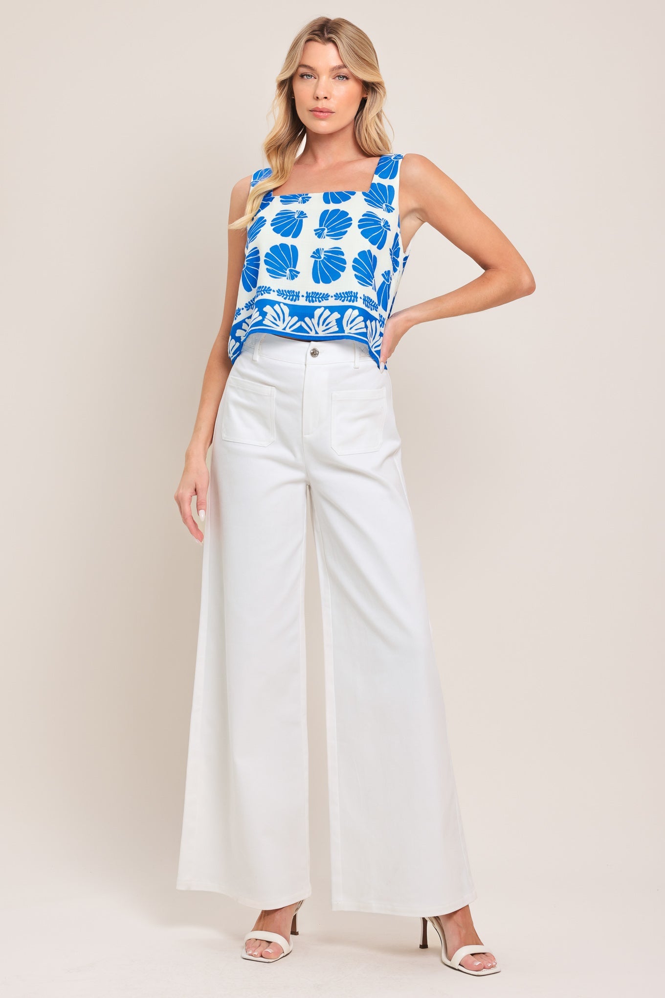 Woman wearing a blue floral top and white pants on a plain background