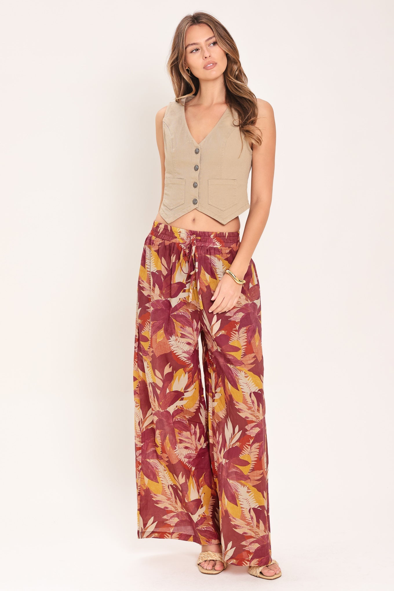 Woman wearing a beige vest and patterned pants on a white background