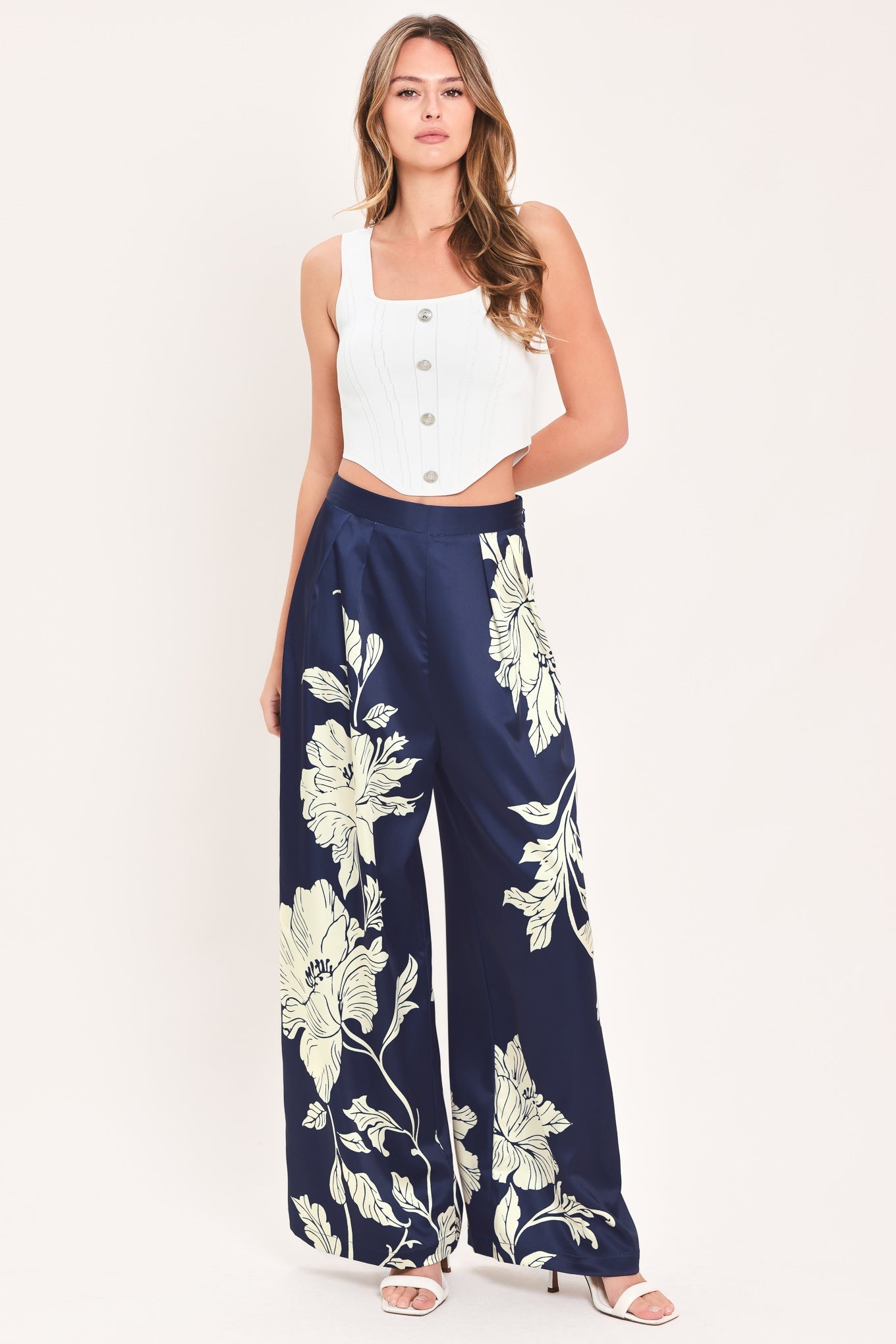 A woman modeling a sleeveless white crop top and navy wide-leg pants with a large cream floral print, standing against a plain light background.
