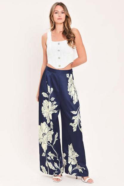 A woman modeling a sleeveless white crop top and navy wide-leg pants with a large cream floral print, standing against a plain light background.
