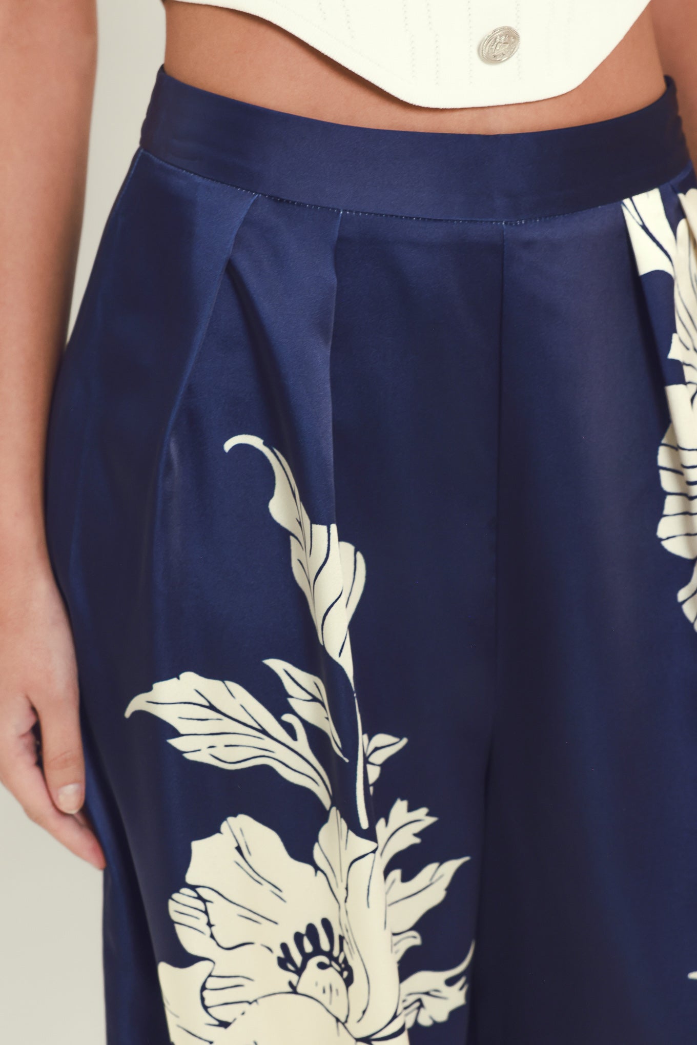 Close-up of a model wearing navy blue wide-leg trousers with a large white floral print, paired with a white cropped top.