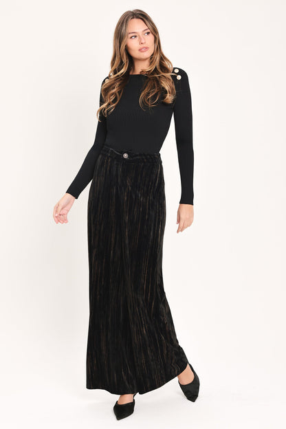 A woman modeling a black long-sleeve knit top with decorative buttons on the shoulders and a matching high-waisted, pleated black maxi skirt, paired with black pointed-toe heels, against a plain white studio background.