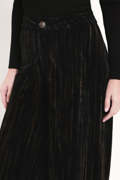 Close-up of a person wearing a black ribbed long-sleeve top and a black pleated velvet skirt with subtle warm brown undertones and a single button closure.
