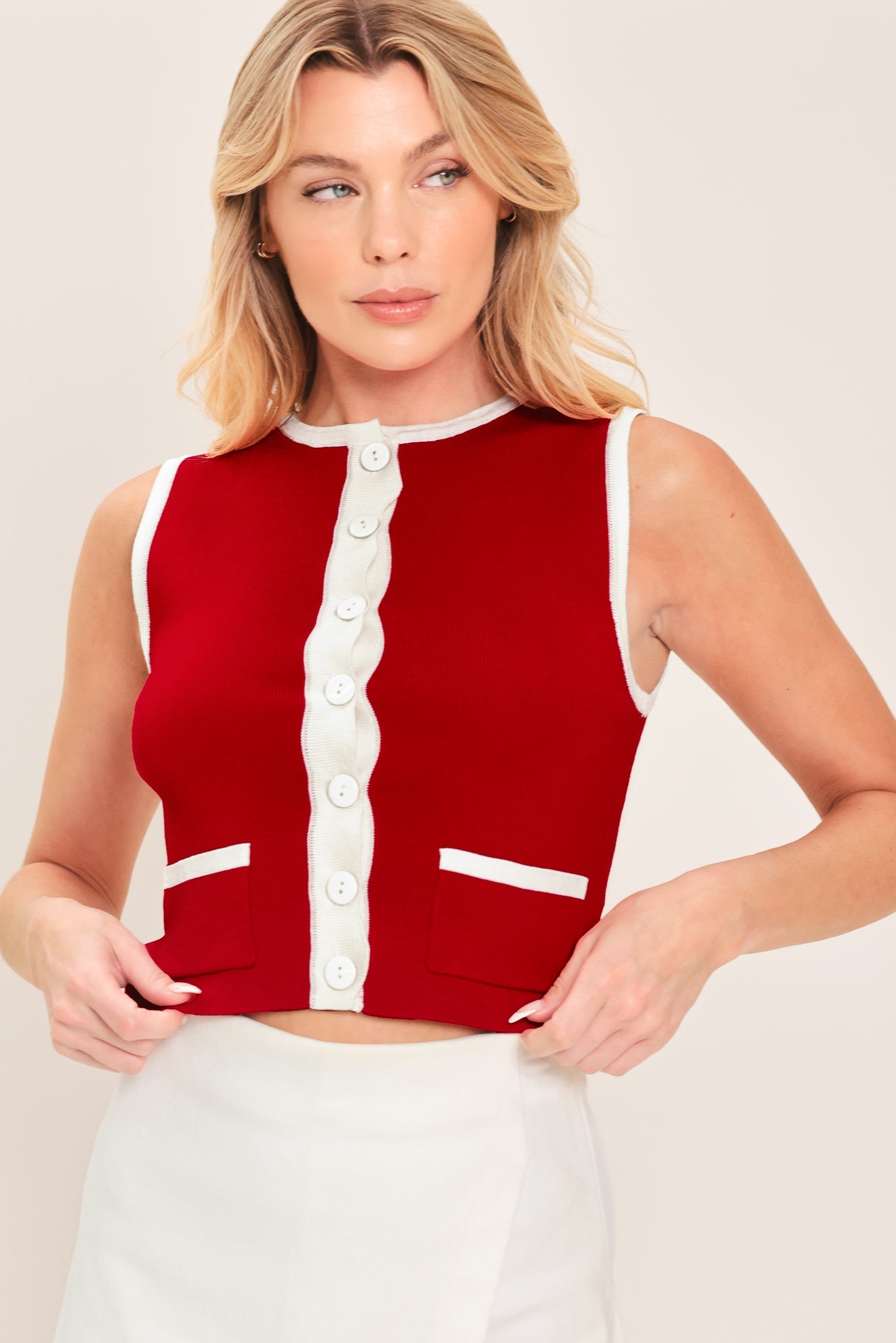 Woman wearing a red sleeveless top with white buttons and trim on a plain background