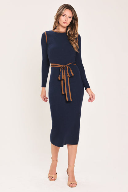A woman modeling a navy blue long-sleeve midi dress with brown trim details on the shoulders and a matching brown tie belt at the waist, set against a plain light beige background.