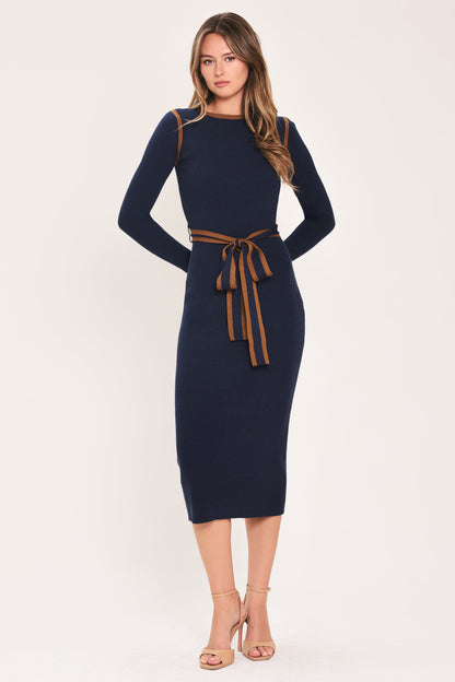 A woman modeling a navy blue long-sleeve midi dress with a brown tie belt at the waist, paired with beige high-heeled sandals, against a plain light beige studio background.