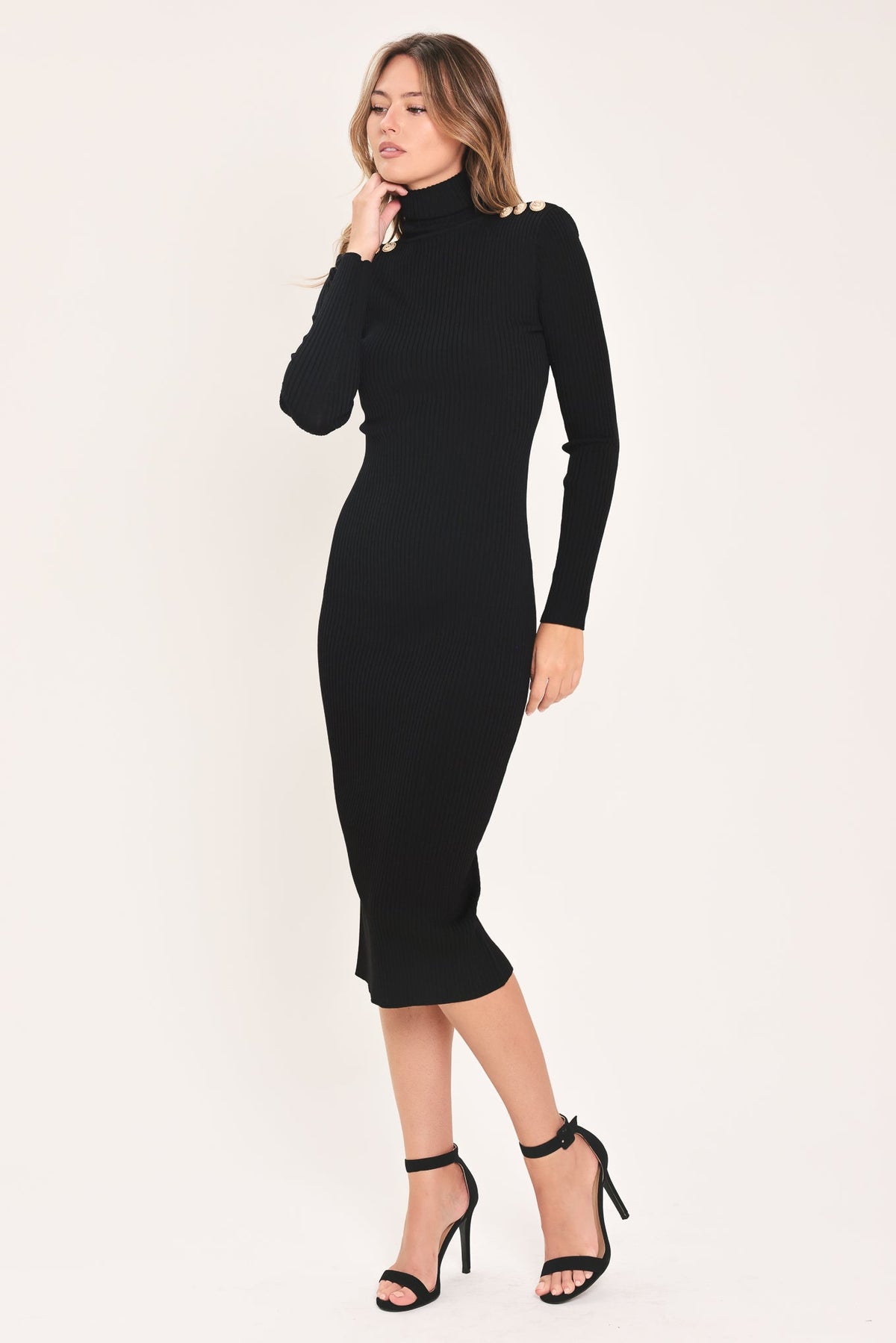 Model wearing a fitted black turtleneck sweater midi dress with gold shoulder buttons and black heels, angled front view.