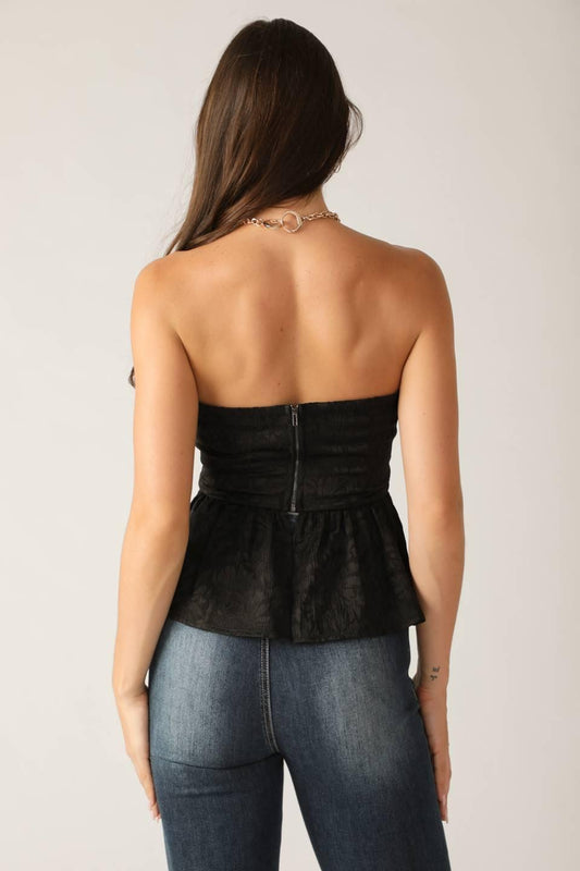 Person wearing a black strapless top and blue jeans against a plain background