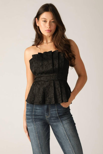 Woman wearing a black peplum top and blue jeans on a plain background